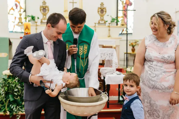 papa qui penche l'enfant au dessus du baptistère et le prêtre verse l'eau