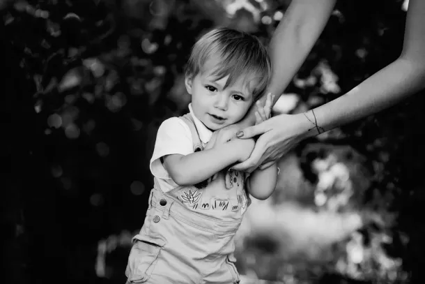 photo en noir et blanc d'un petit garçon timide qui tient la main de sa maman