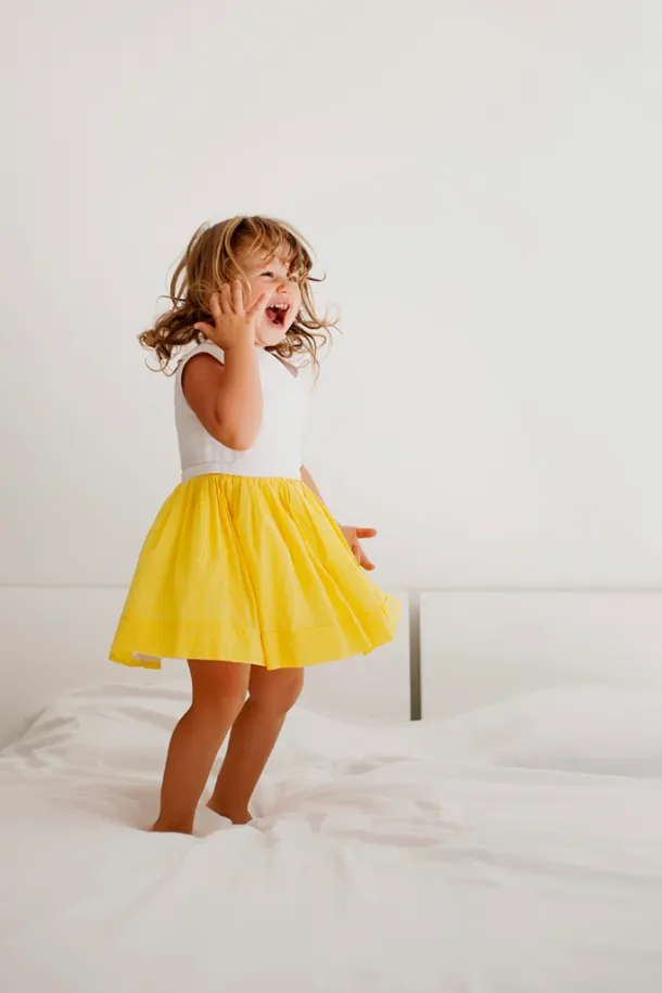 photo lifestyle à domicile d'une petite fille en robe jaune qui sautent sur un lit